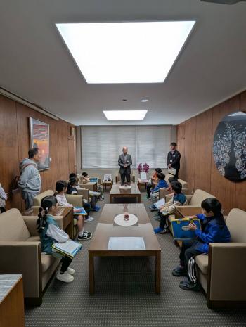 部屋のいすに座るこどもたちと、立って話をする男性