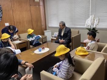 黄色い帽子を被ったこどもたちが男性の話をメモしている