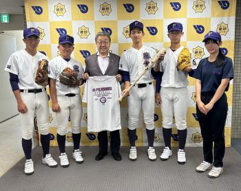 パネルの前で野球のユニフォームを着る生徒とスーツを着た大人