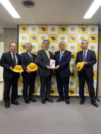 パネルの前で黄色い帽子も持って立つ男性たち