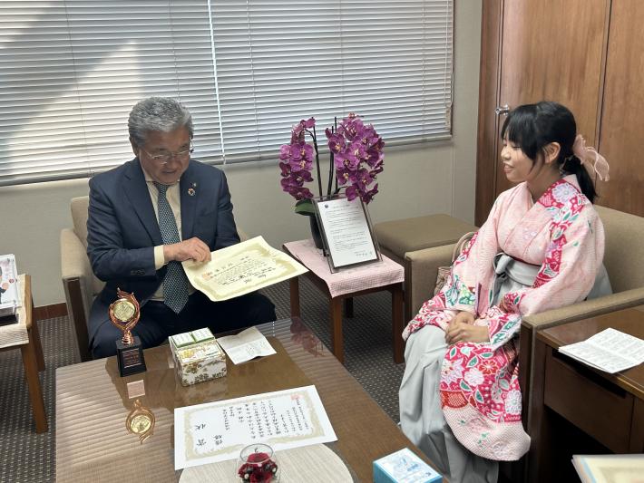 机に並べれた賞状と盾を眺める男性と女性