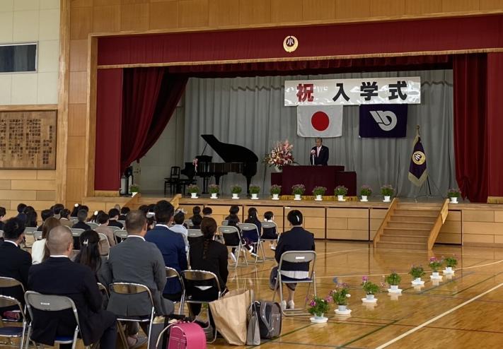 祝入学式と書かれた看板の下からあいさつをする男性