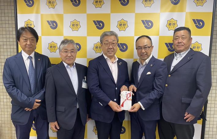 目録をもって立つ男性のまわりを囲んで立つ男性たち