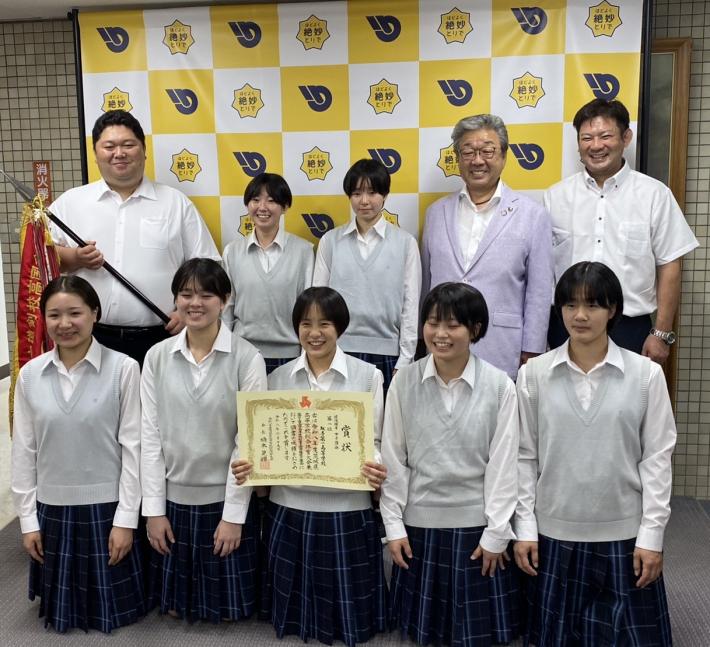 制服を着てパネルの前に立つ女子中学生とスーツを着た男性たち