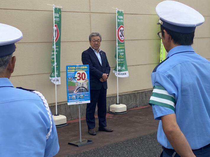 制服を着た交通安全指導隊の前であいさつをする男性