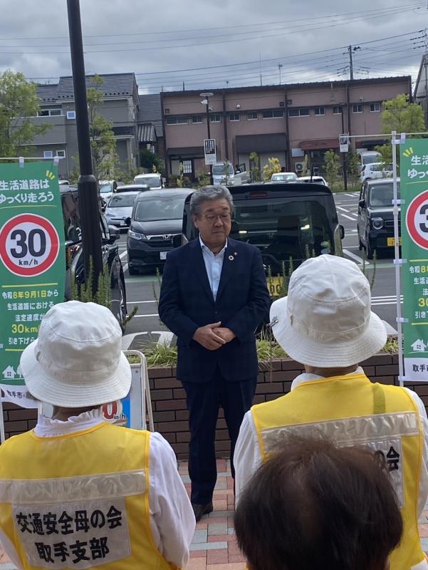 交通安全母の会と書かれた服を着た人たちにあいさつをする男性