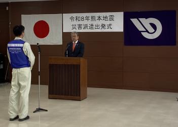 日本国旗の取手市旗の前に立つスーツを着た男性と作業着の男性