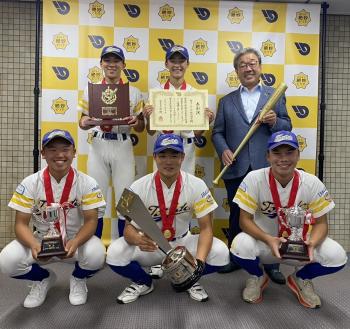 野球ユニフォームを着た中学生とスーツを着た男性がパネルの前で立っている