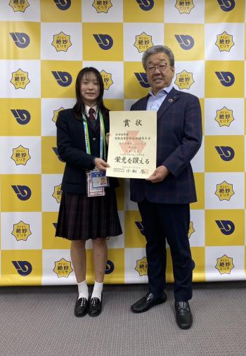 パネルの前に立つスーツを着た男性と制服を着た女子学生