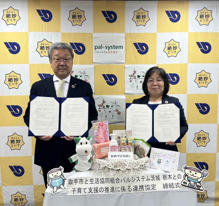 パネルの前に立つ男女がそれぞれ協定書をもっている