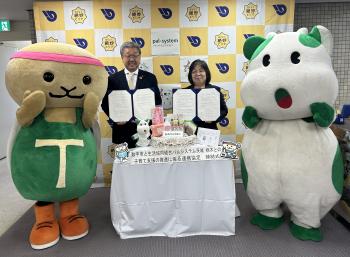 パネルの前に立つ着ぐるみ2体と男女