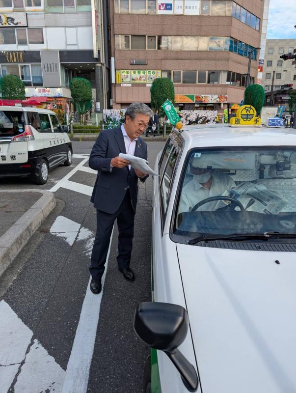 白い車の利用者に啓発品を配る男性