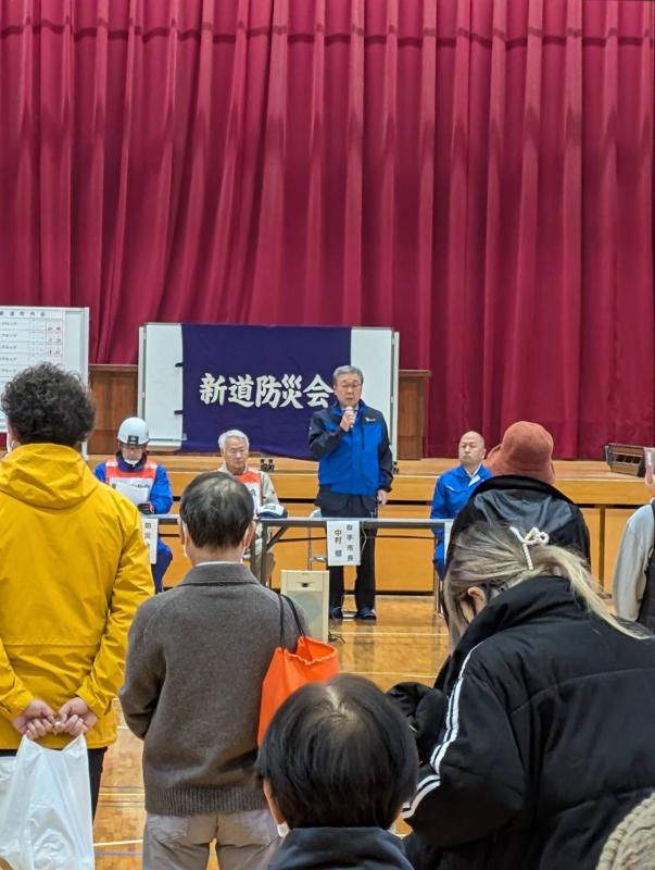 体育館内で防災服を着てあいさつをする男性