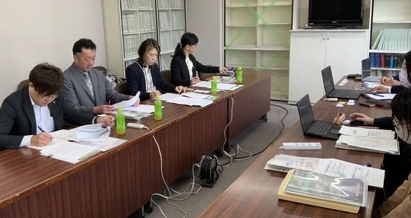 男性と女性の議員が座って、資料を見ながら話を聞いている