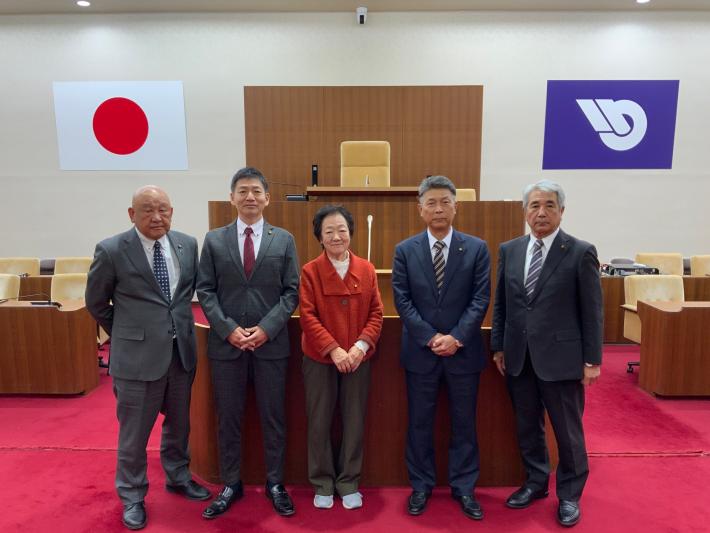 議場で男女数名の議員が立って横に並んでいる