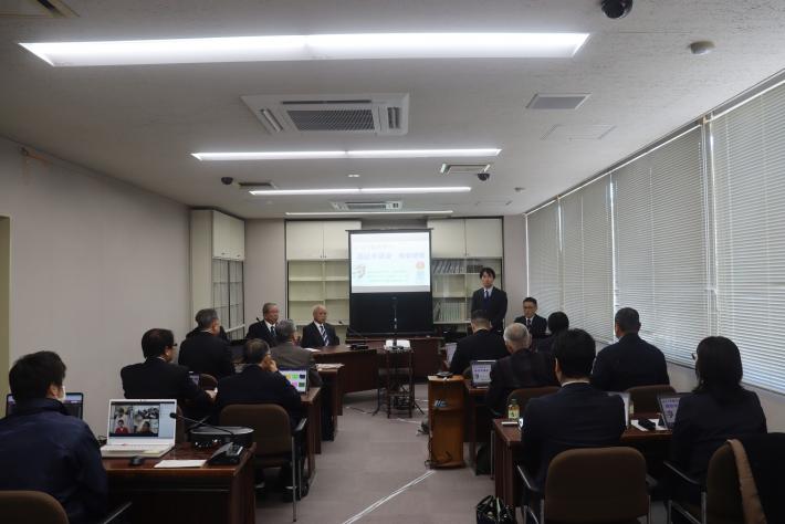 会議室のスクリーンを見ながら数名の議員が机に座っている