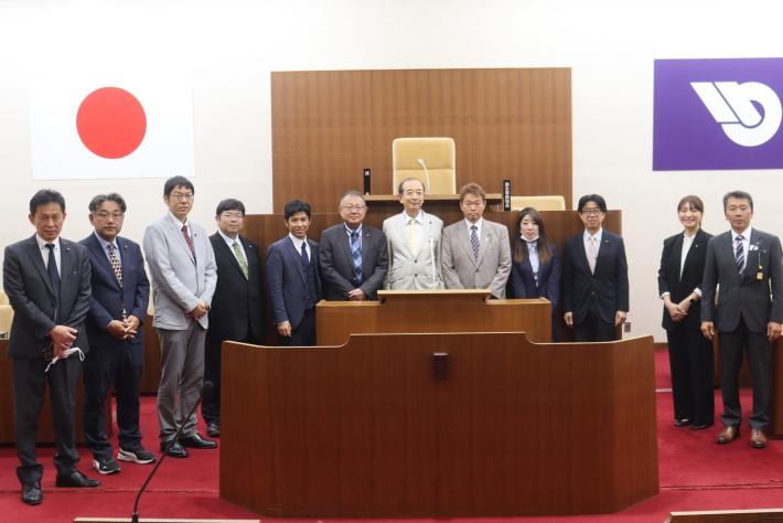 議場で男性と女性の議員数名が立って並んでいる