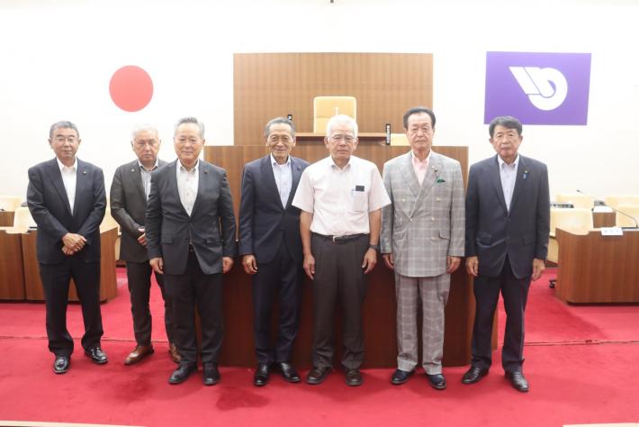 市議会議場で男性の議員数名が立って並んでいる
