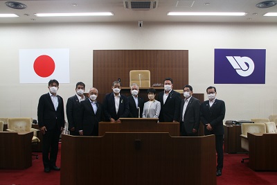 8人のスーツを着た男性議員と1人の白い服を着た女性議員が横一列に並んでいる。中央に金澤議長と根岸議員がいる。