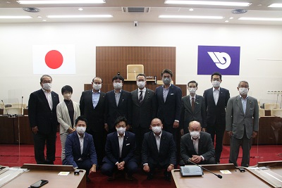 議場の演台前での集合写真。前列に男性4人が、後列左から赤羽・根岸委員、上田市議6人、鈴木委員が立つ