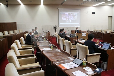 議場に6人の議員が座り、それぞれが手元のタブレットでオンライン会議に参加。顔の脇で手を挙げている