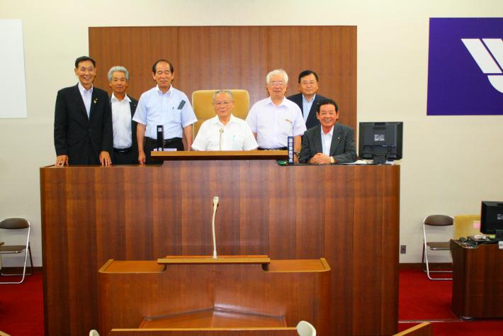 議長席に上がり、横一列で記念撮影をする四国中央市の議員7人の写真