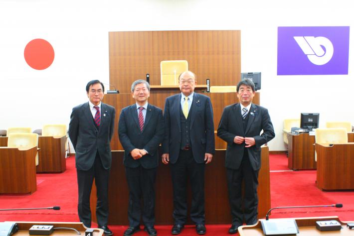議長席前に、スーツを着た短髪の男性が横一列に並び、笑顔でこちらを向いている。奥の壁には取手市のマークと日本の国旗が飾られている