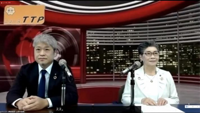 Zoom画面上にてニューススタジオのバーチャル背景を背に、白髪のスーツを着た男性と短髪の女性がテーブルに座っている