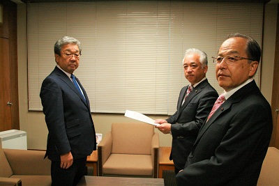 会議室内に、スーツを着た短髪の男性3名がこちらを向いて立っている。そのうち1人は紙を手に持っている
