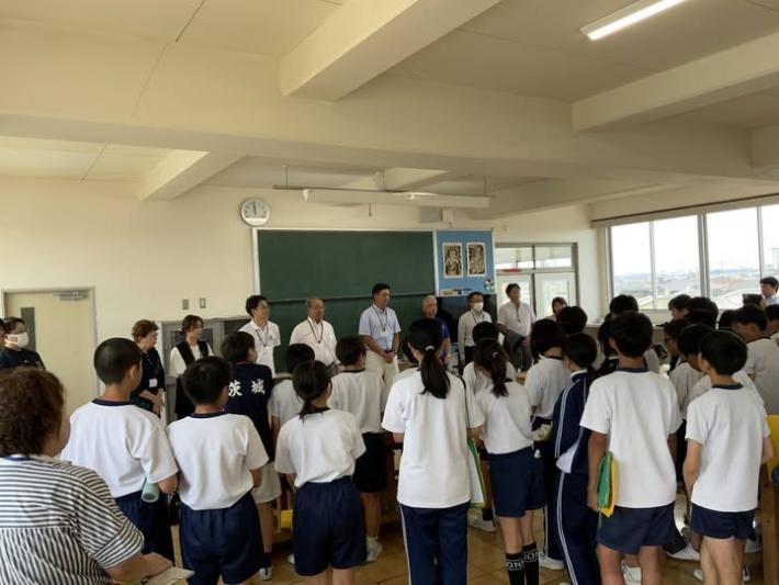 小学校の教室で、黒板の前に男女の議員数名が並び、それを数十名の生徒が見ている