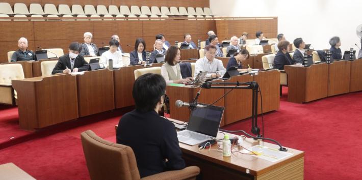 議場で男女数名の議員が男性講師の話を座って聞いている
