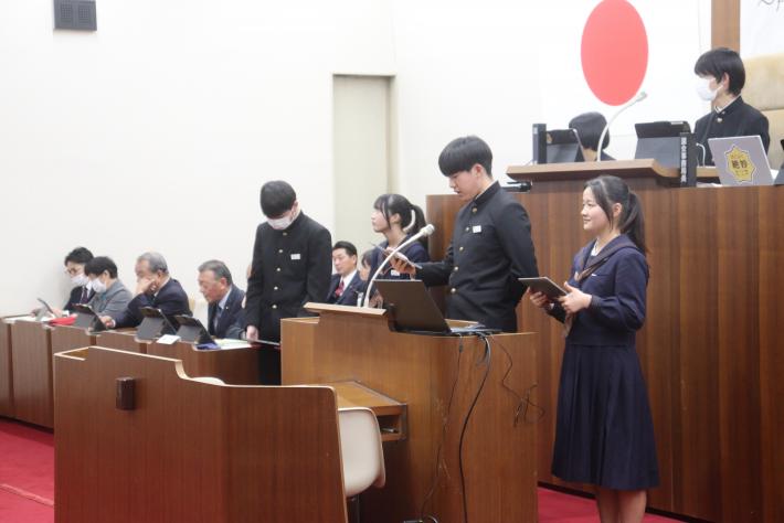 1組の生徒が壇上に上がり発表をしている様子とその奥で発表を聞く議員たち