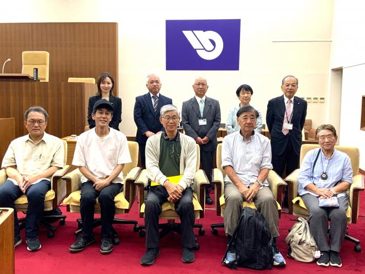 議場で男女の議員と市民数名が並んいる