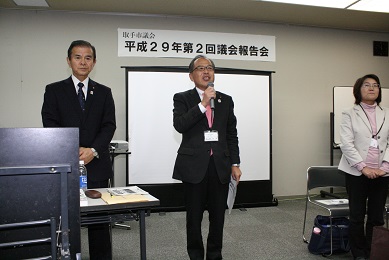 スクリーンの前で3人の議員が立っている。中央の男性議員(染谷副議長)が挨拶をしている写真。