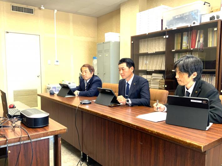 会議室で議員が机に座って、パソコンに向かってオンラインで参加した市民から意見を聞いている