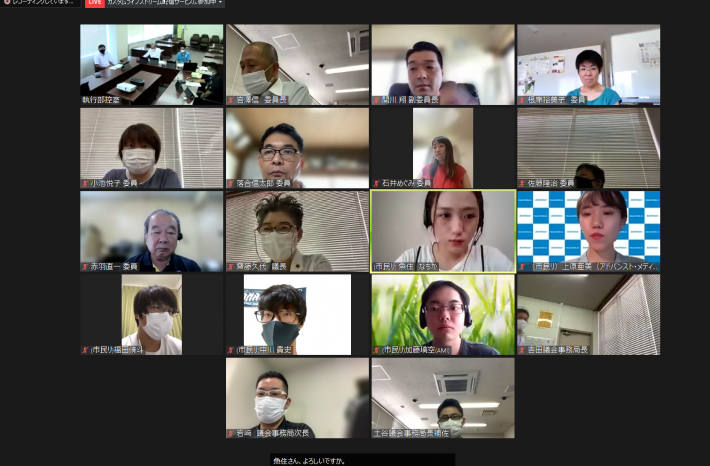 16分割されたZoom画面上に会議室の映像、男性と女性16名が映り、会議をしている