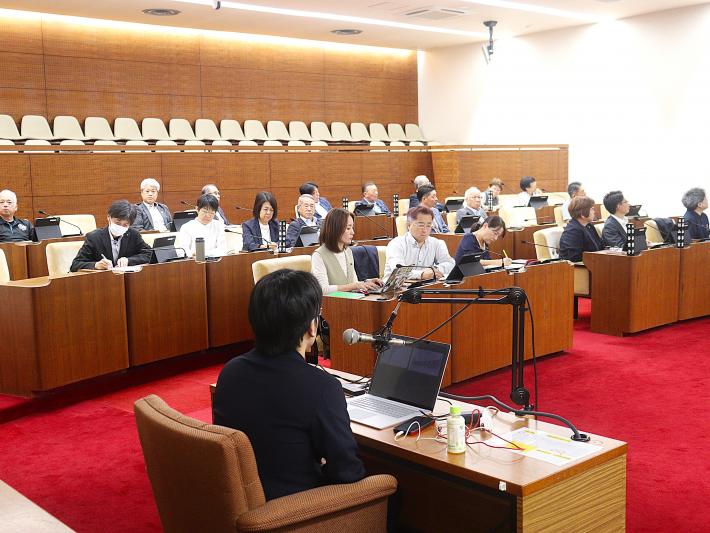 男性の研修講師が座って21名の議員に説明を行っている