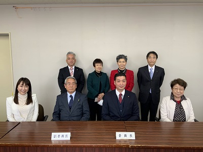 前列に4人が着席、後列に4人が立つ。前列の中央右に男性委員長、中央左に男性副委員長が座り、その左右に女性委員が座る。