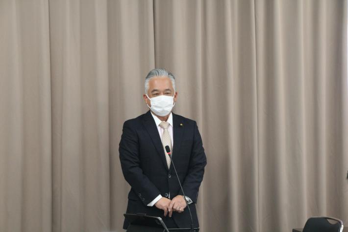 白髪スーツを着た男性議長が開会の挨拶をする写真