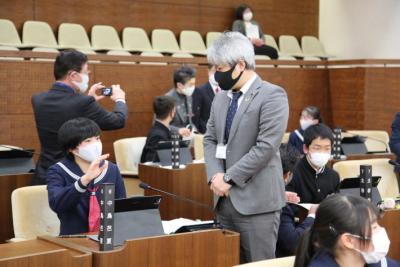 灰色のスーツを着た男性議員に質問する女性生徒議員の写真