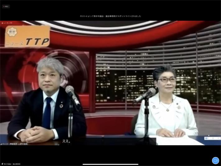 Zoom画面上にてニューススタジオを背景に白髪のスーツを着た男性と短髪の女性がテーブルに座っている