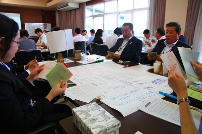 様々なことが書かれた模造紙が中央にあり、その周りに議員と職員が座る。それぞれが手元のカラフルなカードを見ている
