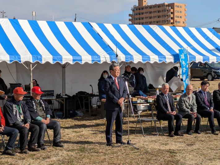 屋外にて青と白の縦縞のテントの前であいさつをする市長