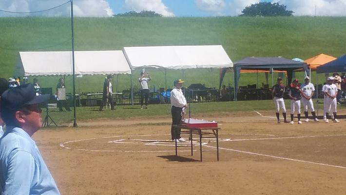 交流自治体少年野球交流大会開会式での市長あいさつ。ホームベース位置に立つ男性の姿。背景に白テントとユニフォーム姿の子どもたち