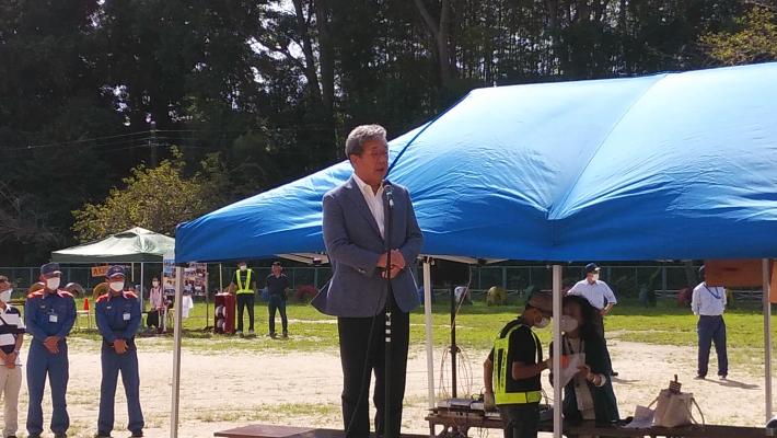 校庭でテント前の演台上でマイクで話をする市長