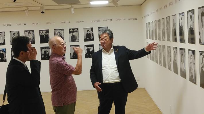 壁に展示された写真を見る市長、副市長と間に写真展主催者。