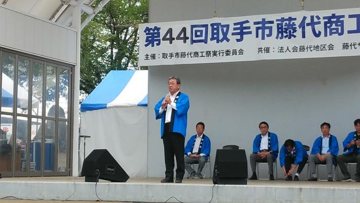青いはっぴを着用した市長がステージ上で挨拶をしている