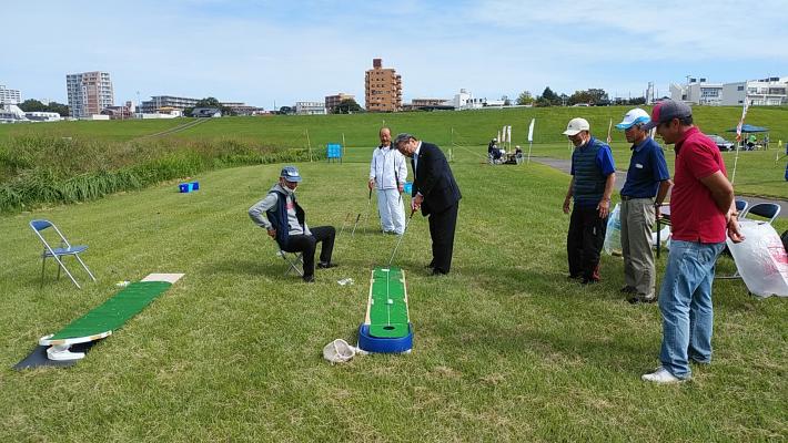 芝生の広場でグラウンドゴルフの体験をする市長と見守る市民
