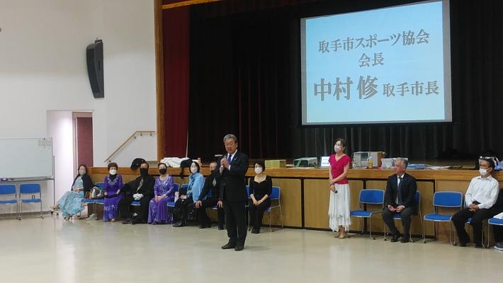 ホールにてステージ前で挨拶をする市長。市長の後ろにはダンスのドレスを着た参加者