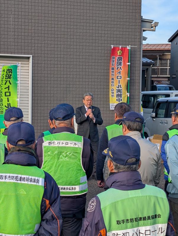 防犯チョッキを着た参加者に向けてあいさつをする男性